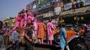 Umat Hindu berkerumun di sekitar mobil Rolls Royce 1921 yang dimodifikasi membawa patung dewa Krishna melalui bangunan bersejarah Howrah Bridge selama festival Holi di Kolkata, India, Minggu, 5 Maret 2023. (AP Photo/Bikas Das)