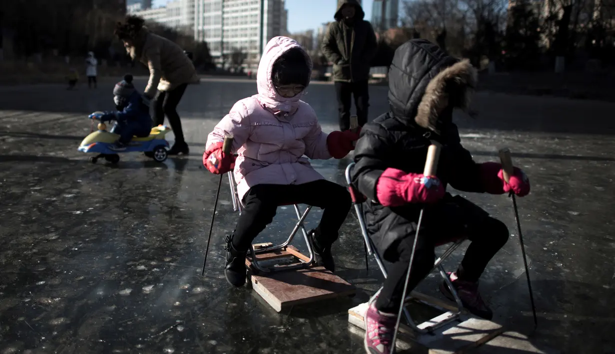 Sejumlah anak bermain di sungai yang membeku di Beijing, China (21/1). Akibat membeku, Sungai ini menjadi objek wisata dadakan yang banyak diminati wisatawan. (AFP/Fred Dufour)