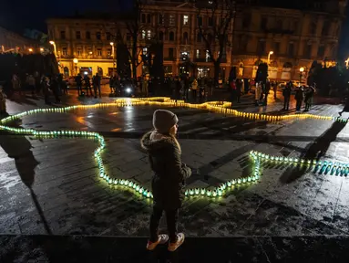 Seorang gadis berdiri di depan lilin yang menyala membentuk peta Ukraina di depan monumen Taras Shevchenko, di Lviv, Ukraina barat, Selasa malam (5/4/2022). Orang-orang Ukraina berkumpul untuk momen menghormati nyawa yang hilang dalam perang. (AP Photo/Nariman El- Mofty)