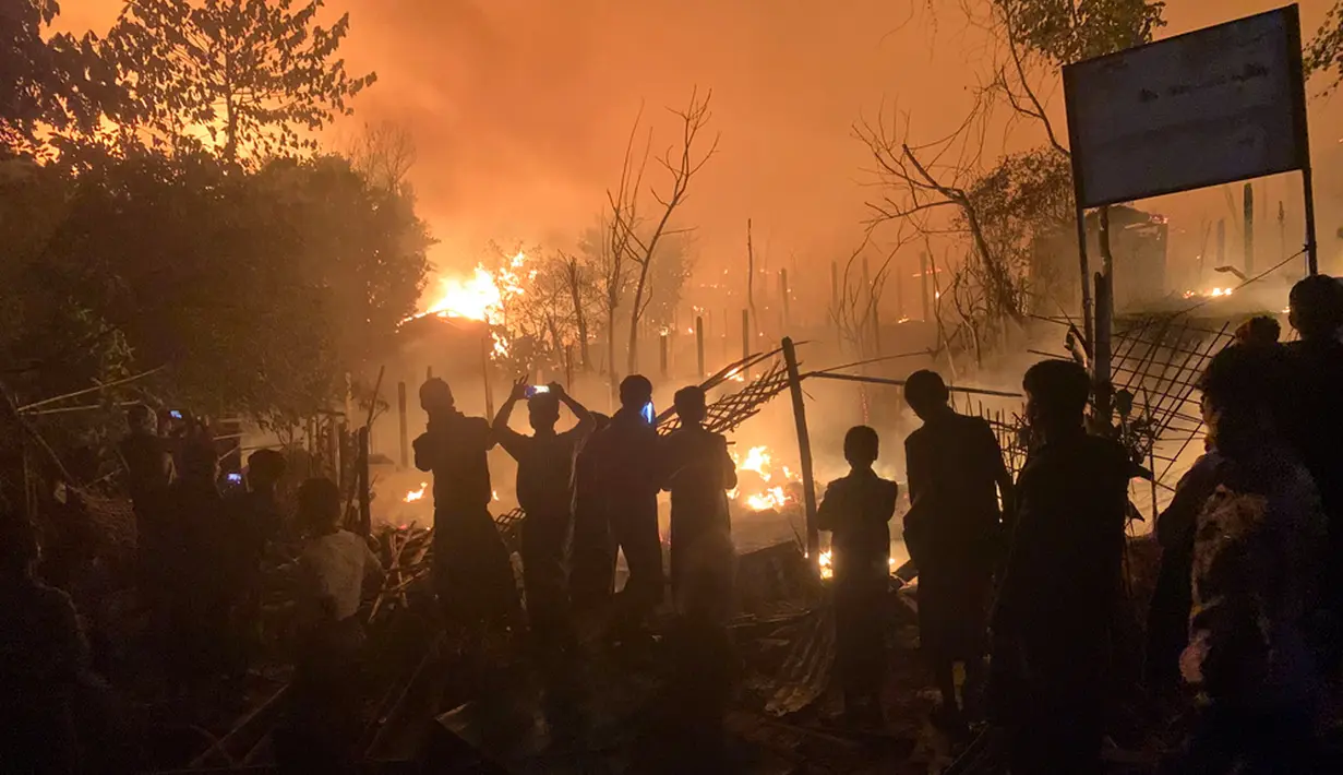 Orang-orang menyaksikan api muncul dari kebakaran di kamp pengungsi Rohingya di Kutupalong. (AP Photo/Shafiqur Rahman)