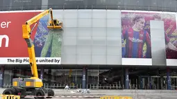 Pekerja menghapus poster yang menampilkan pemain depan Barcelona asal Argentina Lionel Messi di stadion Camp Nou di Barcelona (10/8/2021). Para pendukung PSG berharap untuk melihat pemain asal Argentina itu bergabung ke klub milik Qatar setelah hengkang dari Barcelona. (AFP/ Pau Barrena)