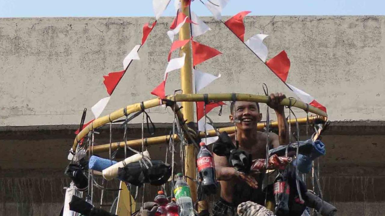 Senyum semringah seorang peserta yang berhasil mencapai puncak pohon pinang.