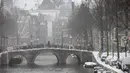 Seorang pria melintasi jembatan di Distrik Lampu Merah yang hampir kosong di Amsterdam, saat salju dan angin kencang menyelimuti sebagian besar wilayah Belanda, Minggu (7/2/2021). Peringatan bahaya cuaca ekstrem telah dikeluarkan oleh pihak BMKG Belanda. (AP Photo/Peter Dejong)