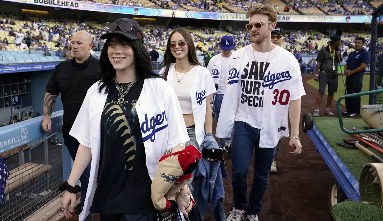 Penyanyi Billie Eilish (kiri) dan saudara laki-lakinya Finneas O'Connell (kanan) berjalan di lapangan sebelum pertandingan bisbol antara Los Angeles Dodgers dan San Francisco Giants di Los Angeles, Amerika Serikat, 21 Juli 2022. Penyanyi asal Amerika Serikat ini tampak antusias menyemangati tim lokal Los Angeles Dodgers. (AP Photo/Marcio Jose Sanchez)