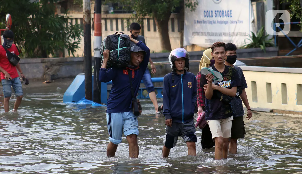 Warga berjalan melintasi genangan banjir rob yang menggenangi kawasan Pelabuhan Nizam Zachman, Muara Baru,  Jakarta, Jumat (5/6/2020). Banjir rob di Pelabuhan Muara Baru tersebut terjadi akibat cuaca ekstrem serta pasang air laut. (Liputan6.com/Helmi Fithriansyah)