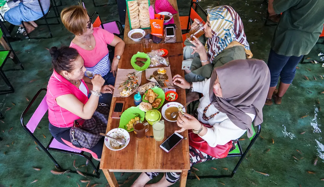 Pengunjung menikmati makan siang sambil digigit ikan dikakinya di restoran kolam ikan di desa Wedomartani di Yogyakarta (15/11/2019). Restoran unik ini dikenal dengan nama Soto Cokro Kembang. (AFP Photo/Oka Hamied)