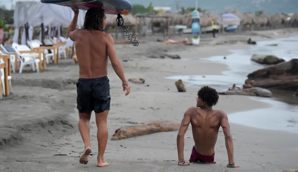 Imigran Venezuela, Alfonso Mendoza alias Alca (kanan) berjalan di pantai usai bermain surfing di Puerto, Kolombia, 27 September 2018. Musik dan teman membantunya untuk lebih optimis menjalani hidup. (Raul ARBOLEDA/AFP)