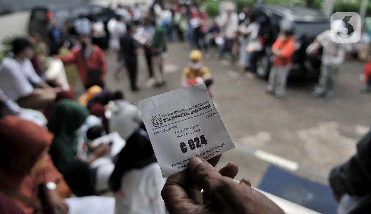 Warga menunjukkan nomor saat mengantre di Kantor Suku Dinas Dukcapil Jakarta Timur, Senin (15/6/2020). Layanan tatap muka Dukcapil Jakarta Timur yang kembali dibuka sejak Jumat (12/6) lalu disambut antusias warga yang ingin mengurus dokumen administrasi kependudukan. (merdeka.com/ Iqbal S Nugroho)