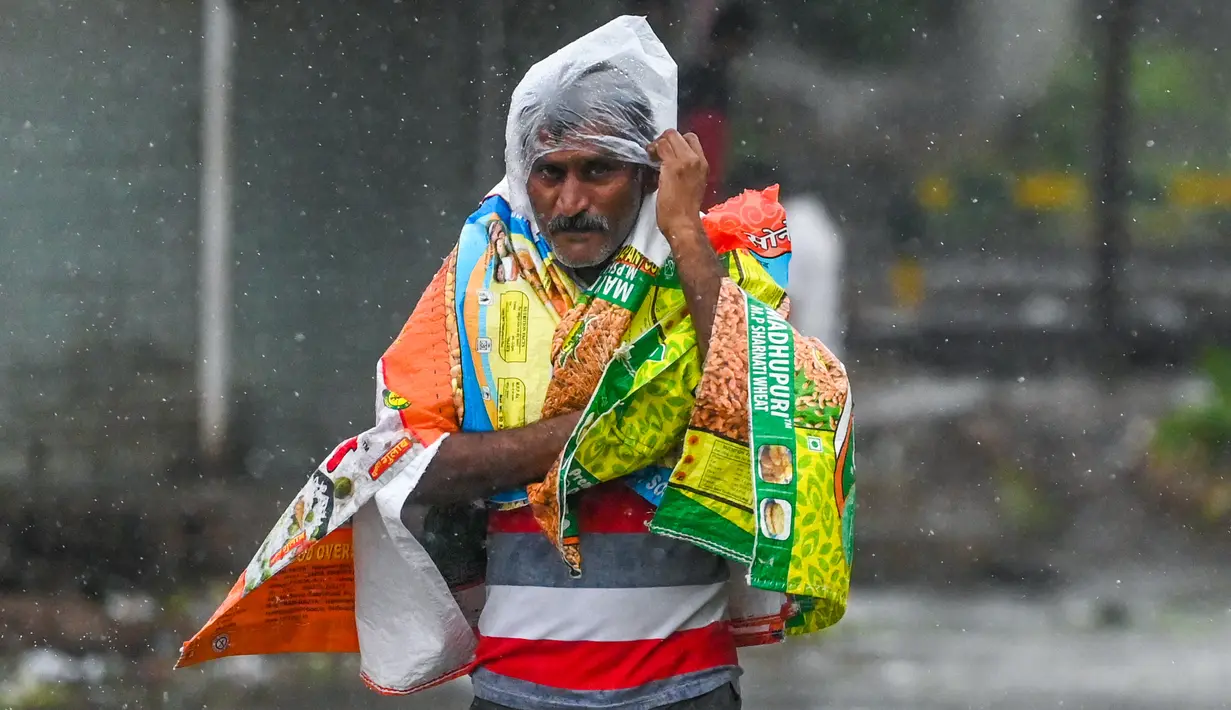 Seorang pria menutupi dirinya dengan plastik saat berjalan di sepanjang jalan di Amreli setelah siklon Tauktae menghantam pantai barat India pada Selasa (18/5/2021). Topan Tauktae disebut yang terbesar melanda wilayah itu dalam beberapa dekade terakhir. (Punit PARANJPE / AFP)