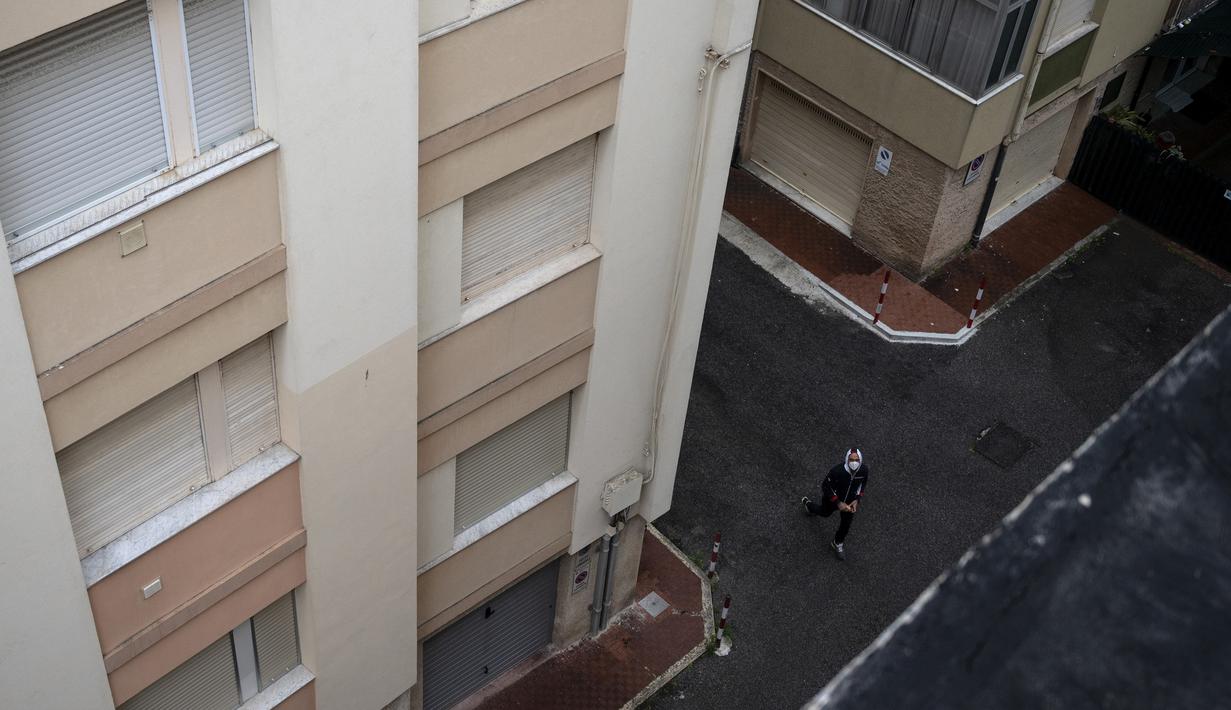 Ayah Vittoria Oliveri mengenakan masker wajah, mengumpulkan bola tenis di halaman ketika putrinya dan seorang temannya berlatih tenis di atap rumah mereka di Finale Ligure, Wilayah Liguria, Italia barat laut (19/4/2020). (AFP/Marco Bertorello)