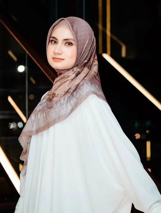 Raisya Bawazier tampil menawan mengenakan gamis berwarna putih dipadukan scarf bermotif warna coklat muda. [@snap.nuel/@rezartemeviaofficial/@ochiipramita]
