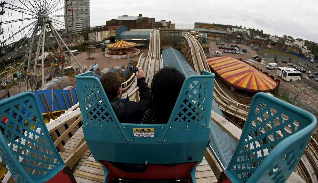 Pengunjung mengabadikan gambar mereka saat mencoba The Scenic Railway atau roller coaster kayu di Dreamland, Inggris, Kamis (15/10/2015). Roller coaster ini sudah ada sejak tahun 1920. (REUTERS/Stefan Wermuth)
