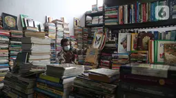 Pedagang bermain ponsel saat menunggu pembeli buku di Pasar Kenari, Jakarta, Rabu (24/11/2021). Semua toko yang berada di lantai 3 merupakan toko subsidi dari pemerintah.  (Liputan6.com/Faizal Fanani)