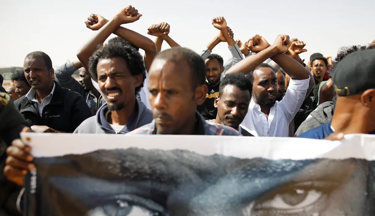 Migran Afrika membawa poster dan foto rekan mereka yang tahan pemerintah Israel saat melakukan aksi di Penjara Saharonim, Israel (22/2). Ratusan imigran Afrika di pusat penahanan Holot juga telah memulai aksi mogok makan. (AFP Photo/Menahem Kahana)