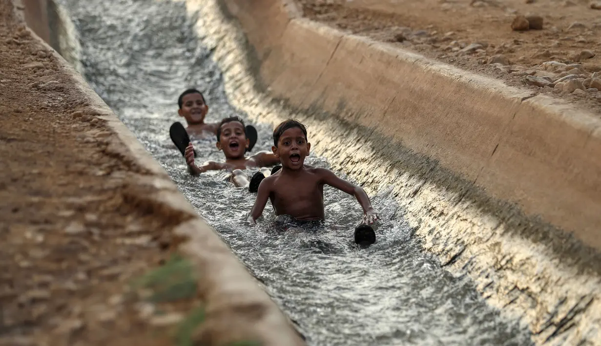 Anak-anak bermain di aliran mata air yang digunakan untuk irigasi untuk mendinginkan tubuh saat suhu udara mencapai 44 derajat Celcius di kota Jericho, Tepi Barat (1/9/2020). (AFP Photo/Ahmad Gharabli)