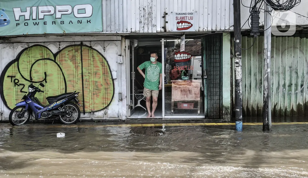 Warga berada di depan toko saat banjir menggenangi Jalan Jatinegara Barat, Jakarta, Senin (8/2/2021). Ketinggian air yang menggenangi Jalan Jatinegara Barat mencapai setinggi paha orang dewasa, sehingga menyebabkan kemacetan. (merdeka.com/Iqbal S. Nugroho)