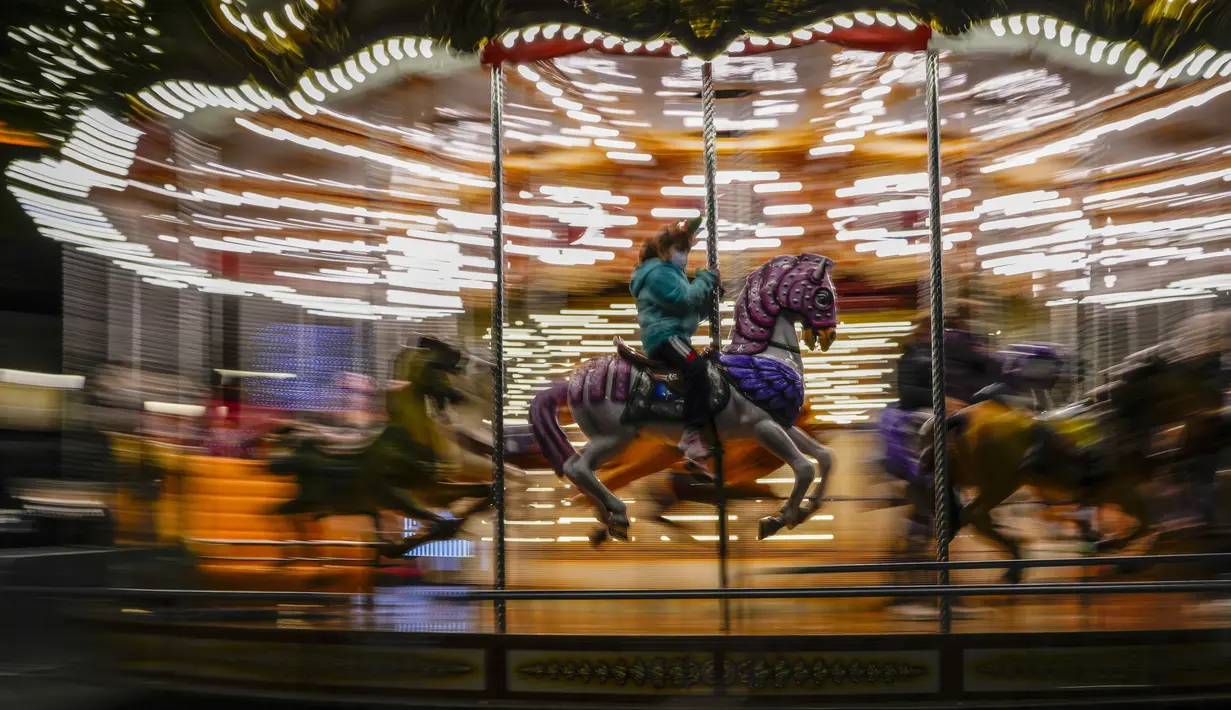 Seorang anak menaiki komidi putar di pameran Natal di pusat kota Madrid, Rabu (22/12/2021). PM Spanyol Pedro Sanchez mengadakan rapat Kabinet khusus untuk mengesahkan undang-undang yang mewajibkan penggunaan masker di luar ruangan di tengah lonjakan rekor kasus COVID-19. (AP Photo/Manu Fernandez)