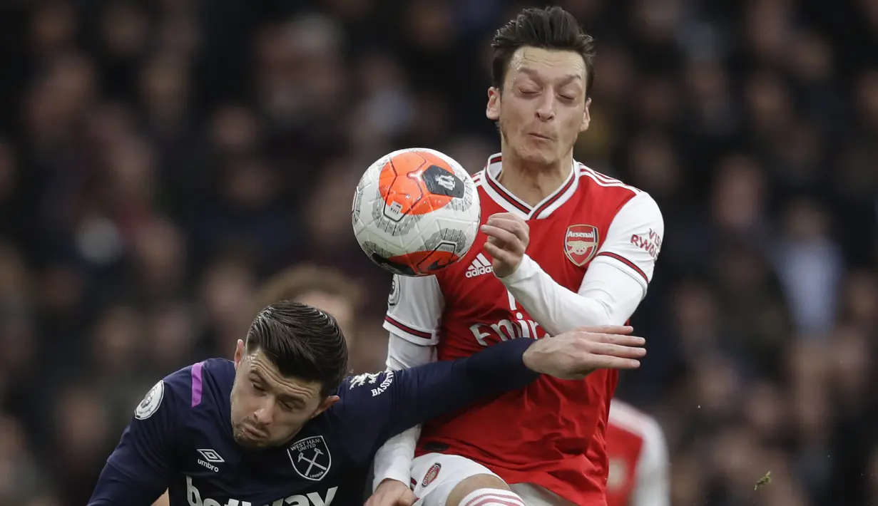 Pemain Arsenal, Mesut Ozil, duel udara dengan pemain West Ham United, Aaron Cresswell, pada laga Liga Inggris di Stadion Emirates, Sabtu, (7/3/2020). (AP Photo/Matt Dunham)