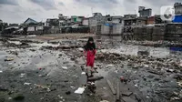 Seorang anak melintasi genangan sampah di permukiman kumuh Muara Baru, Jakarta, Rabu (19/1/2022). Badan Pusat Statistik (BPS) mencatat angka kemiskinan Indonesia turun menjadi 26,5 juta orang per September 2021 dari sebelumnya mencapai 27,54 juta orang pada Maret 2021. (merdeka.com/Iqbal S Nugroho)
