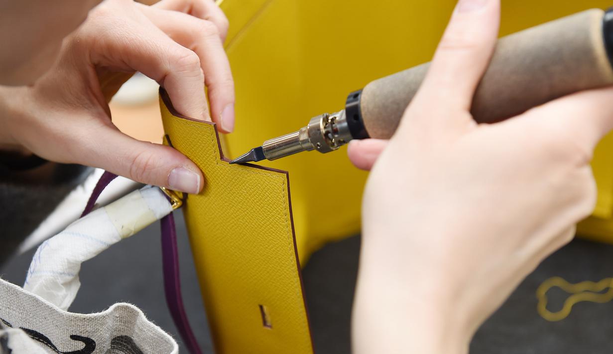 Seorang pengrajin merapikan bagian tas saat bekerja di bengkel produsen barang-barang mewah Hermes di Allenjoie, Perancis, Kamis (5/4). Tas Hermes dijual dengan harga ratusan hingga miliaran rupiah. (SEBASTIEN BOZON/AFP)