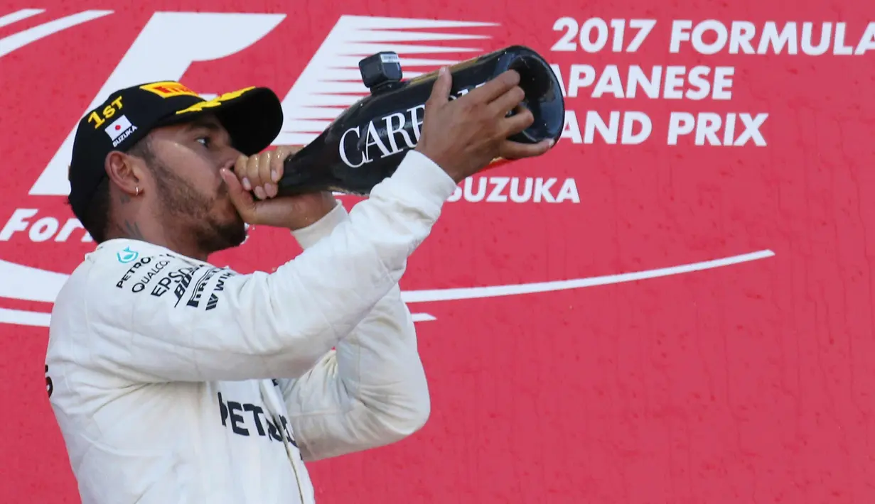 Lewis Hamilton meminum sampanye di atas podium merayakan kemenangannya pada GP F1 Jepang di Sirkuit Suzuka, Jepang, (8/10). Hamilton mengoleksi 306 poin atau unggul 59 poin dari Vettel yang gagal finis di Suzuka. (AP Photo / Toru Takahashi)