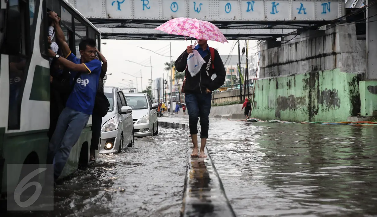 Seorang pejalan kaki sambil menggunakan payung melintasi banjir yang menggenangi jalan di depan Ancol, Jakarta, Kamis (21/4). Hujan deras yang mengguyur sejak semalam menyebabkan beberapa kawasan di Jakarta tergenang banjir. (Liputan6.com/Faizal Fanani) 
