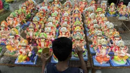 Seorang anak melukis patung Dewa Ganesha yang dipajang untuk dijual di kios pinggir jalan di Hyderabad, India, Kamis (9/9/2021). Patung dewa Hindu berkepala gajah tersebut banyak dijual jelang Festival Ganesh Chaturthi. (NOAH SEELAM/AFP)