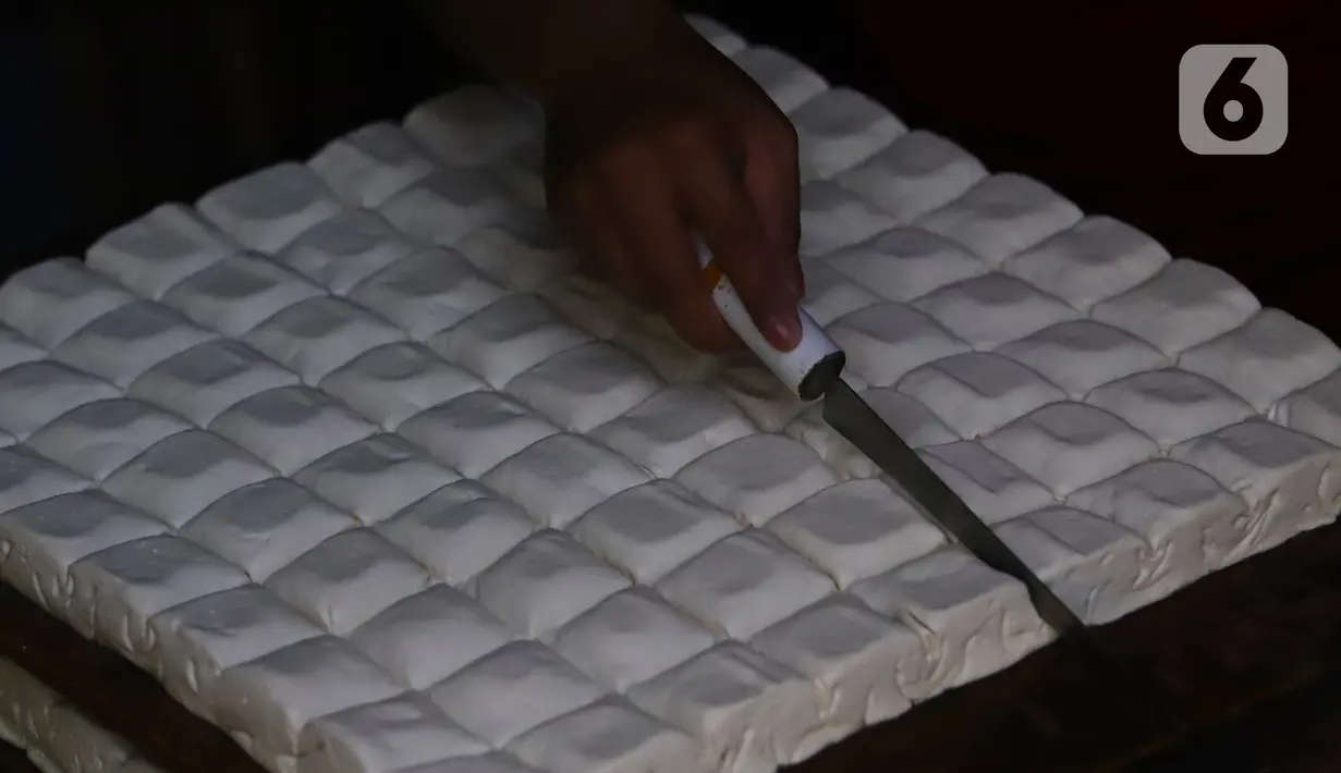 Pekerja memotong tahu dari kedelai di Jakarta, Senin (4/1/2021). Setelah melakukan mogok produksi selama 1 hingga 3 Januari 2021 akibat naiknya harga kacang kedelei impor, kini para perajin tahu mulai kembali beroperasi. (Liputan6.com/Angga Yuniar)