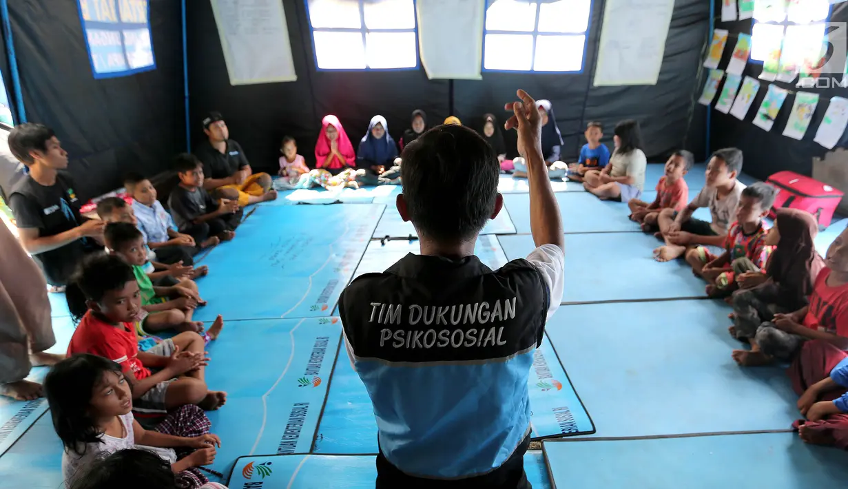 Seorang tim dukungan Psikososial bermain bersama anak-anak korban gempa tsunami Palu di halaman kantor Dinas Sosial Palu, Sulawesi Tengah, Sabtu (6/10). Trauma healing dilakukan agar anak-anak kembali ceria. (Liputan6.com/Fery Pradolo)