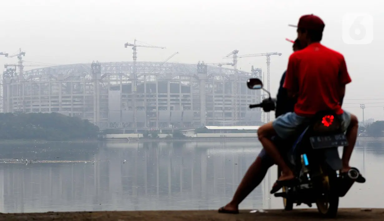 Warga menikmati waktu sore di pinggir Waduk Cincin yang berlatar pembangunan Jakarta International Stadium (JIS), Sabtu (19/6/2021). Pembangunan JIS sudah memasuki tahap pemasangan rangka atap dengan bentang mencapai 269 meter dan ditarget selesai Desember 2021. (Liputan6.com/Helmi Fithriansyah)