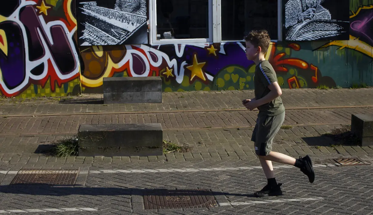 Seorang anak laki-laki melewati grafiti di hari musim semi yang hangat di Amsterdam, Belanda, Selasa (30/3/2021). Kasus COVID-19 di Belanda telah menembus satu juta lebih. (AP Photo/Peter Dejong)