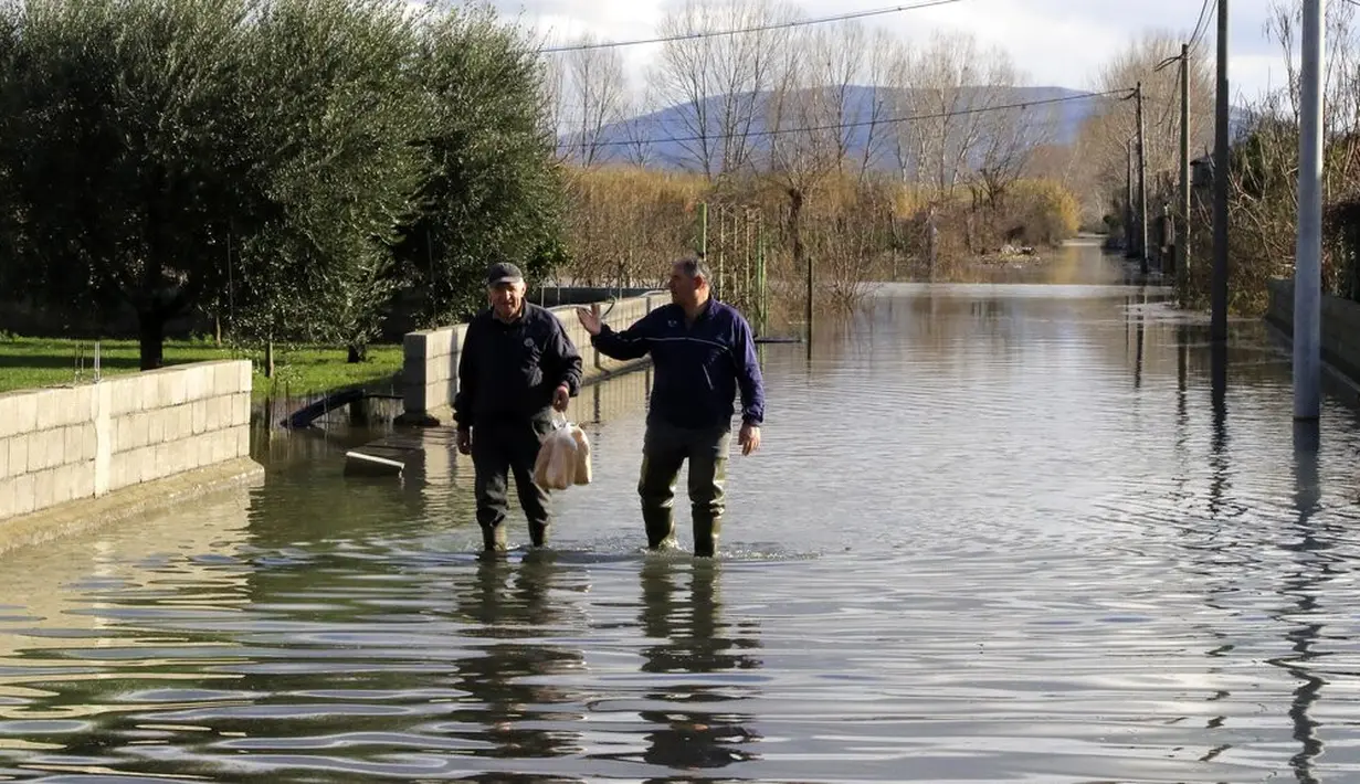 Penduduk setempat berjalan di jalan yang banjir usai hujan lebat di Desa Obot, sekitar 100 kilometer (60 mil) barat laut Tirana, Albania, Senin (11/1/2021). Hujan deras dan salju selama beberapa hari terakhir telah membanjiri banyak kawasan di Albania. (AP Photo/Hektor Pustina)