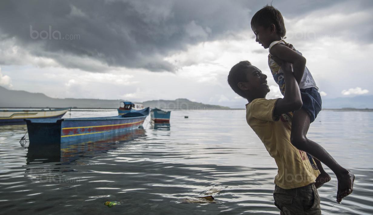 Pesepak bola SSB Tulehu Putra, Alghy Nahumarury, menggendong adiknya saat bermain di belakang rumahnya di Tulehu, Maluku, Selasa (15/11/2017). Meski keadaan sulit, Alghy tetap semangat untuk menjadi pesepak bola. (Bola.com/Vitalis Yogi Trisna)