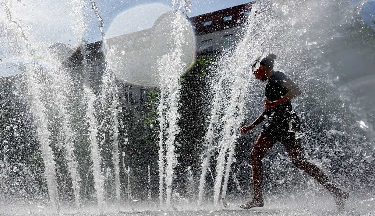 Seorang gadis bermain mendinginkan diri denggan di sebuah fontaine saat gelombang panas menerjang Eropa di Berlin, Jerman, Rabu (24/7/2019 ). Organisasi Meteorologi Dunia (WMO) menyatakan gelombang panas menegaskan dampak dari perubahan iklim. (AP Photo/Michael Sohn)
