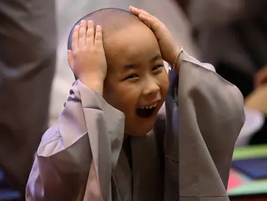 Seorang anak lelaki tertawa memegang kepalanya usai dicukur pada seremonial ulang tahun Buddha di kuil Jogye, Seoul, Rabu (2/5). Sepuluh anak terpilih mendapatkan pengalaman menjadi biksu dalam rangkaian acara peringatan hari lahir Buddha (AP/Lee Jin-man)