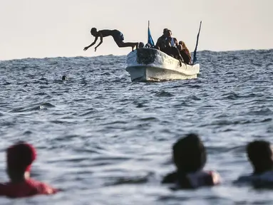 Seorang anak melompat dari sebuah kapal di Pantai Jazera di pinggiran Mogadishu, Somalia (24/11). Pantai ini jadi tempat rekreasi populer bagi warga Somalia. (AFP Photo/Mohamed Abdiwahab)