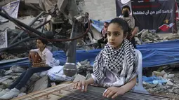 Seorang gadis Palestina memainkan alat musik saat tampil di puing-puing Menara Hanadi di Kota Gaza (2/6/2021). Acara diselenggarakan oleh Komite Pemuda dan Kebudayaan Palestina lebih dari seminggu setelah gencatan senjata mengakhiri 11 hari permusuhan antara Israel dan Hamas. (AFP Photo/Mohammed Abe