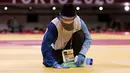 Seorang petugas membersihkan dan mendisinfektan matras pada pertandingan babak penyisihan -81kg judo putra antara Saeid Mollaei dari Mongolia dan Murad Fatiyev dari Azerbaijan selama Olimpiade Tokyo 2020 di Nippon Budokan di Tokyo pada 27 Juli 2021. (Jack GUEZ / AFP)