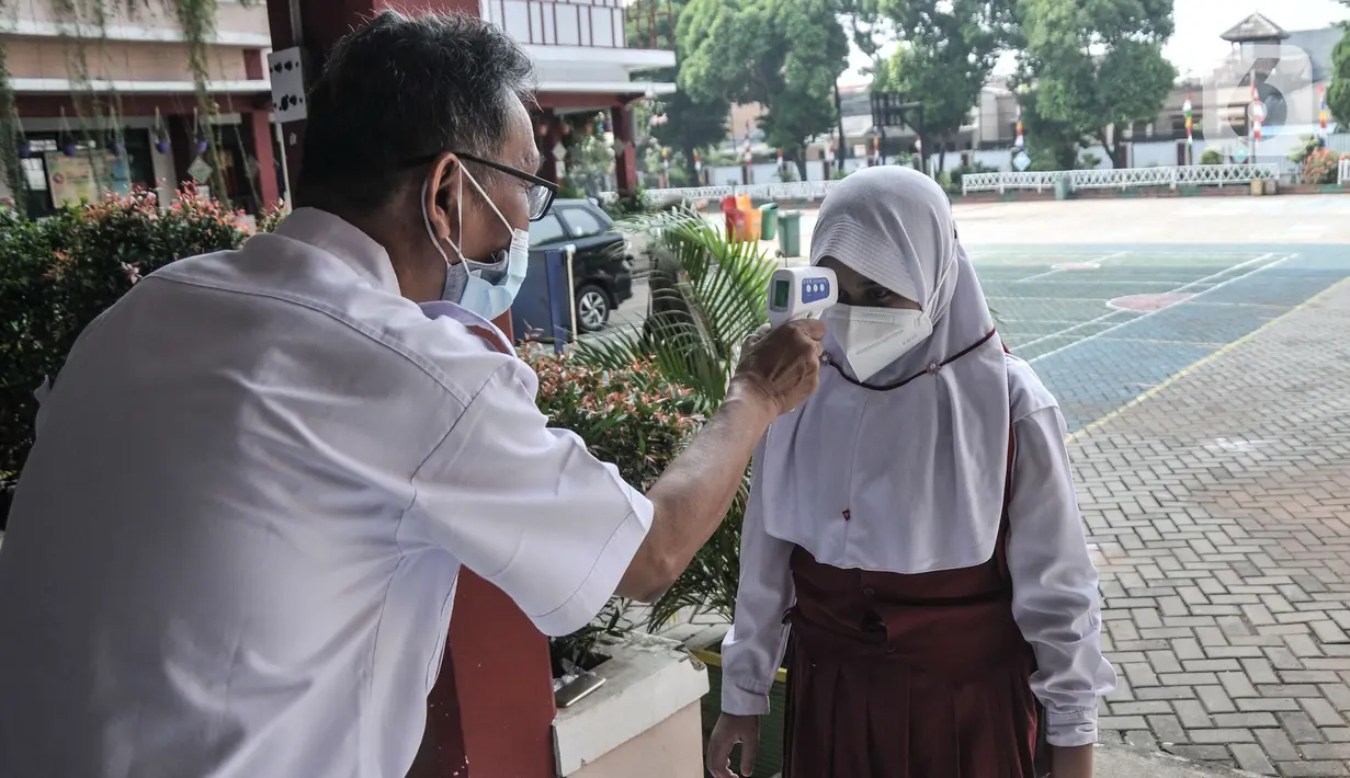Guru memeriksa suhu tubuh murid kelas 1 sebelum mengikuti PTM Terbatas di SDN Malaka Jaya 07 Pagi, Klender, Jakarta, Senin (30/8/2021). Kembali digelarnya PTM hari ini disambut antusias murid, terutama kelas 1 SD yang baru pertama kali belajar langsung di ruang kelas. (merdeka.com/Iqbal S. Nugroho)