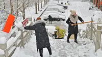 Orang-orang menyekop salju dari jalan layang setelah hujan salju lebat di Yantai, di provinsi Shandong, China timur pada 20 Desember 2023. Suhu di kota-kota di China utara mencapai rekor terendah pada hari Rabu. (STR / AFP)