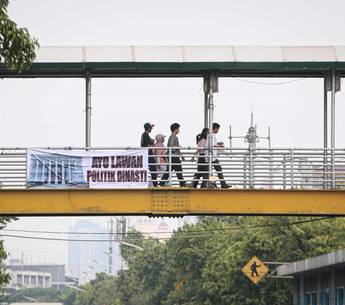 Sejumlah warga berjalan pada jempatan penyeberangan orang yang terdapat sebuah spanduk bertuliskan "Ayo Lawan Politik Dinasti" di Jakarta, Minggu (15/10/2023).
