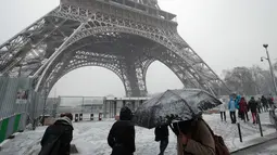 Pejalan kaki berjalan di dekat Menara Eiffel saat turun salju di Paris, Prancis, (6/2). Badan cuaca nasional Prancis Meteo France mengatakan sekitar setengah negara di eropa siaga atas bahaya tingkat salju dan es yang berbahaya. (AP Photo / Francois Mori)