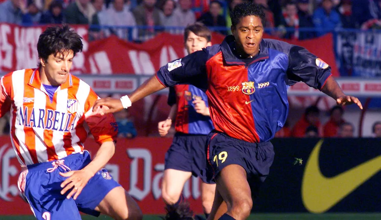 Pemain Barcelona, Patrick Kluivert (kanan) berebut bola dengan pemain Atletico Madrid, Jose Antonio Chamot pada laga lanjutan Liga Spanyol di Madrid, 25 April 1999. Jersey Barcelona musim 1999/2000 terlihat memiliki corak khas Blaugrana, yaitu merah, biru, dan biru tua. Menariknya, terdapat angka tahun 1899 - 1999 yang mengapit logo klub tersebut. (AFP/Eric Cabanis)