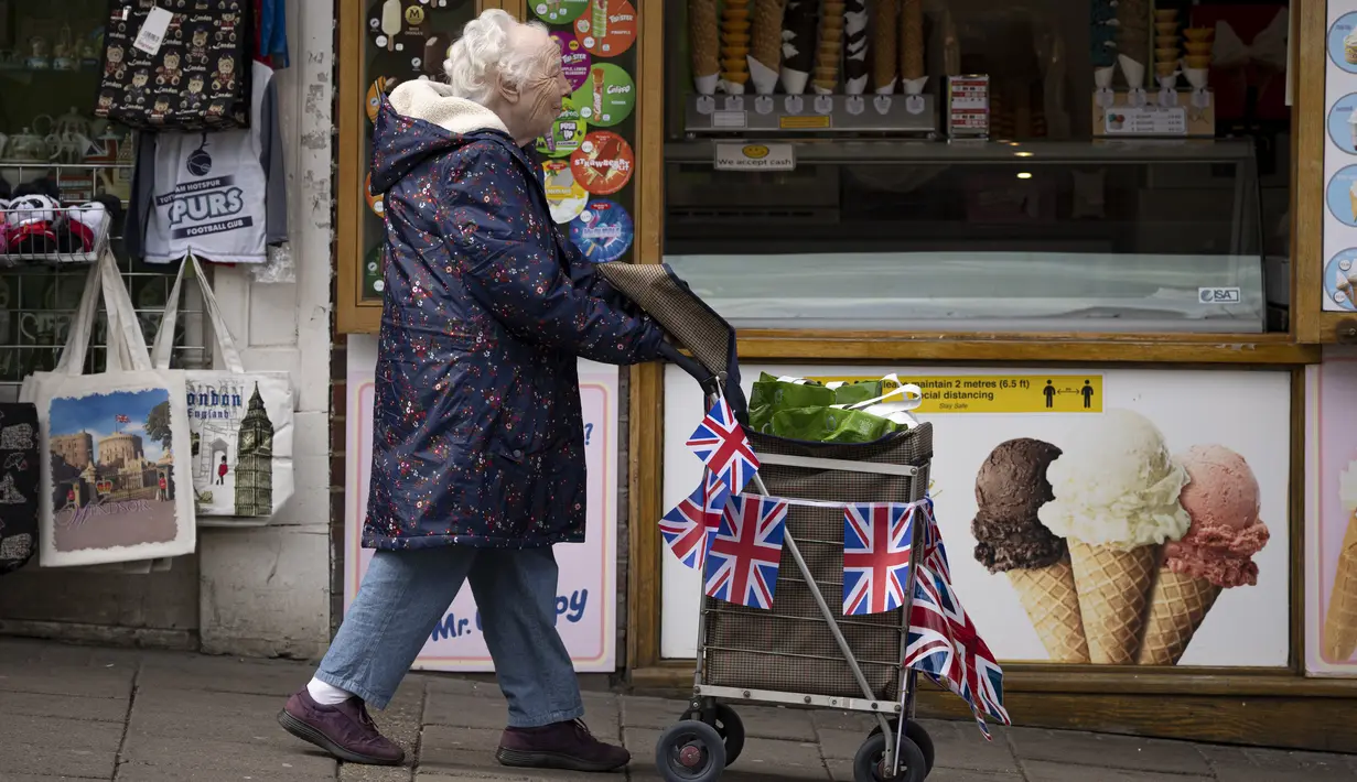 Seorang perempuan mendorong troli berhiaskan bendera Union Jack di Windsor, Jumat, 5 Mei 2023. Penobatan Raja Charles III akan berlangsung di Westminster Abbey pada 6 Mei. (AP Photo/Andreea Alexandru)