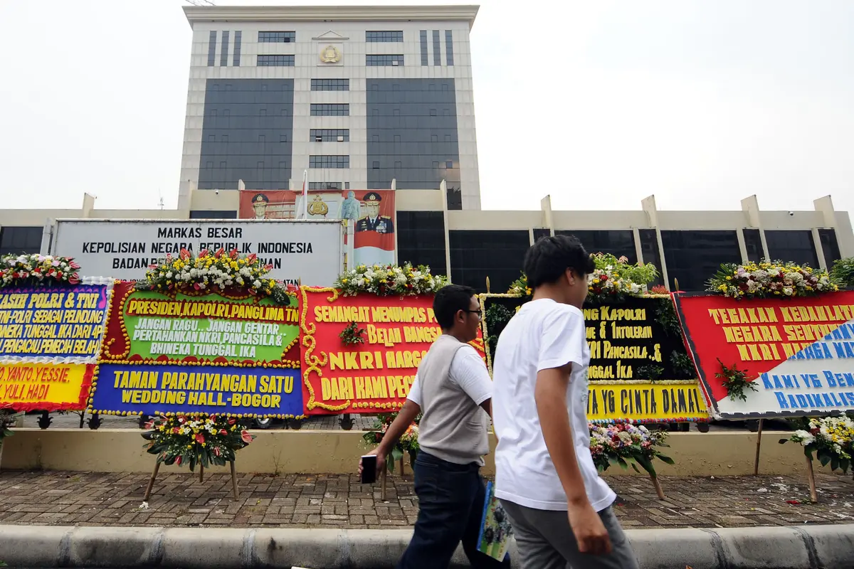 Warga melintasi deretan karangan bunga yang diletakkan di depan Mabes Polri, Jakarta, Rabu (3/5). Ratusan karangan bunga itu terus berdatangan dan mengelilingi gedung Mabes Polri di Jalan Trunojoyo Jakarta Selatan. (Liputan6.com/Helmi Fithriansyah)