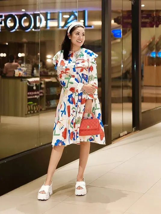 Nindy Ayunda tampil girly dengan collar midi dress berwarna putih. Dress lengan panjang itu dihiasi oleh motif bunga warna-warni yang dipadukan dengan bando dan sandal platform putih serta handbag berwarna merah pastel. (instagram/nindyayunda)