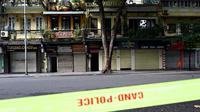 Toko-toko dan restoran-restoran yang tutup terlihat melewati garis polisi di sepanjang jalan yang sepi di Hanoi pada hari pertama lockdown, Sabtu (24/7/2021). Vietnam memberlakukan pembatasan yang lebih ketat di Hanoi akibat gelombang infeksi COVID-19 terburuknya. (Manan VATSYAYANA / AFP)