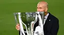 Pelatih Real Madrid, Zinedine Zidane, mengangkat trofi juara La Liga musim 2019/2020 usai timnya mengalahkan Villarreal pada laga lanjutan La liga di Estadio Alfredo Di Stefano, Jumat (17/7/2020) dini hari WIB. (AFP/Gabriel Bouys)