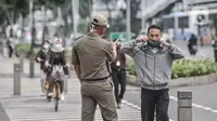 Petugas Satpol PP menegur pekerja yang salah menggunakan masker saat jam pulang kantor di kawasan Sudirman, Jakarta, Senin (14/9/2020). Pengurangan aktivitas pekerja di perkantoran menjadi fokus utama Pemprov DKI Jakarta dalam penerapan PSBB pada 14-27 September 2020. (merdeka.com/Iqbal S. Nugroho)