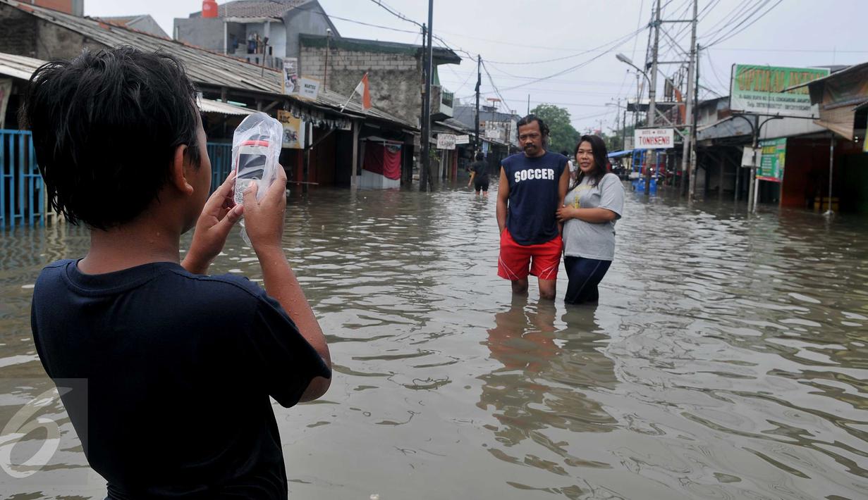 Warga berselfie saat banjir melanda pemukiman warga di Jalan Raya Rawa Buaya, Jakarta, Minggu (28/2/2016). Banjir akibat luapan Kali Mookervart ini menyebabkan ratusan rumah warga tergenang air rata-rata satu meter. (Liputan6.com/Gempur M Surya)
